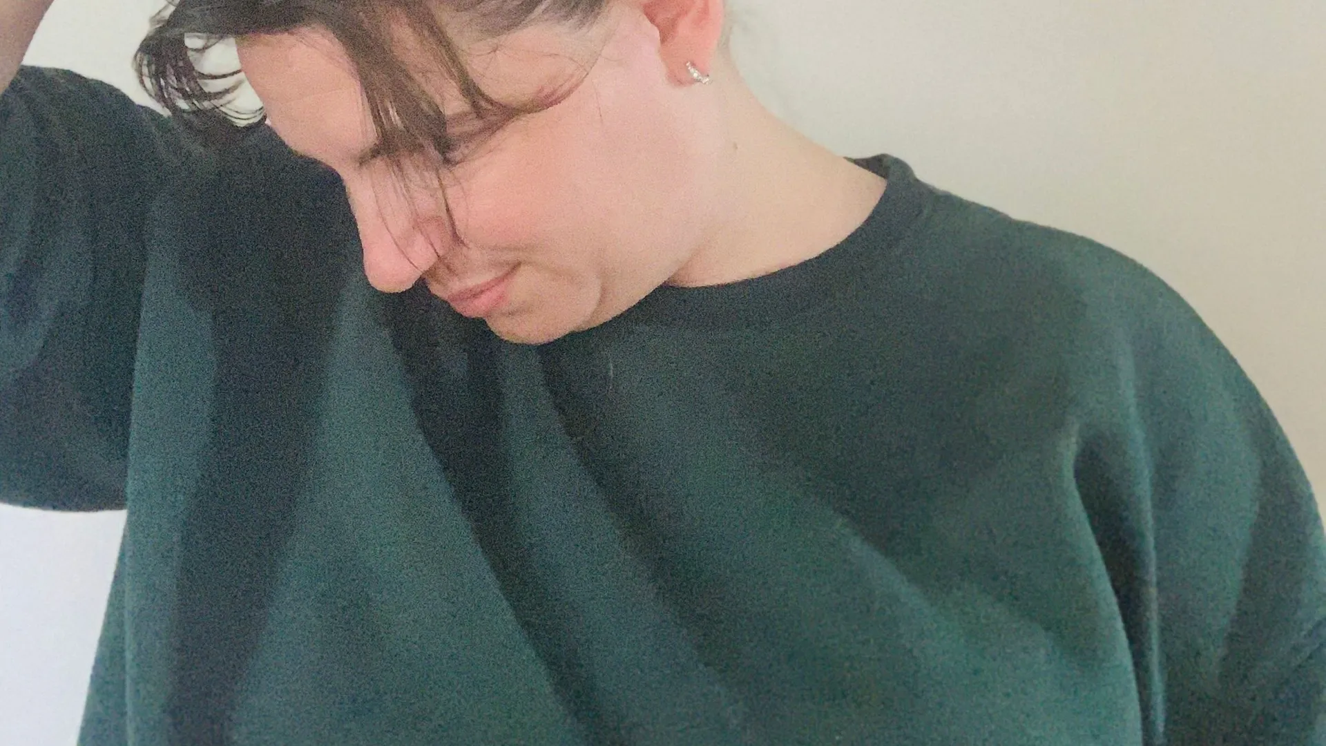 Natalie Brown in a dark green sweatshirt, tilting her head down and to one side with one hand on her head.