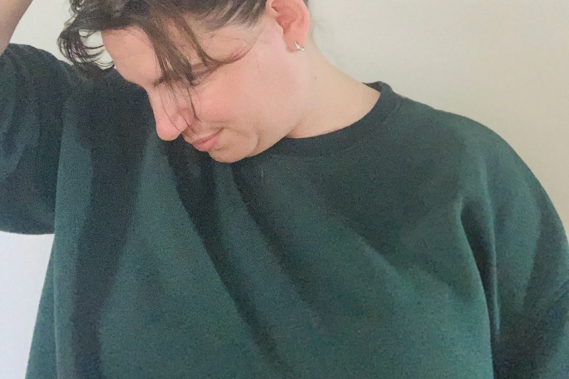 Natalie Brown in a dark green sweatshirt, tilting her head down and to one side with one hand on her head.